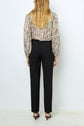 Woman standing with her back to the camera, wearing a floral long-sleeve blouse, a pantalon droit 7/8 à coupe ajustée, and black heels against a plain white background.