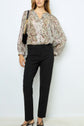 A person wearing a loose, floral-patterned blouse with long sleeves, a pantalon droit 7/8 noir, black heeled sandals, and carrying a black shoulder bag stands against a plain white background.
