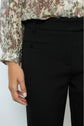 A person wearing a pantalon femme with a coupe ajustée and a long-sleeve floral blouse stands with one hand relaxed at their side.