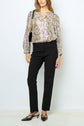 Woman wearing a floral long-sleeve blouse, black heels, and a pantalon droit 7/8 noir à coupe ajustée, holding a black handbag over her shoulder, standing against a plain white background.