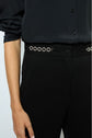 A person wearing a black button-up shirt and high-waisted black pants with a decorative silver chain belt; only the torso and left arm are visible.