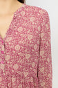 Close-up of a pink crêpe georgette floral-patterned robe courte adorned with cream motif floral designs, featuring a v-neckline and small pink buttons. A portion of the person’s neck, shoulder, and upper chest is visible.
