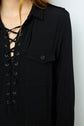 A person wearing a black long-sleeve top with a lace-up V-neck and a buttoned chest pocket, reminiscent of the elegant simplicity of a robe longue noire, shown from the shoulders to the waist.