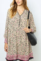 Woman wearing a robe courte à imprimé floral with pink and black accents and long sleeves, holding a black shoulder bag. She has long, light brown hair and is standing against a plain light background.