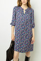 Woman wearing a knee-length, blue motif floral robe courte with three-quarter sleeves, holding a black bag, and black knee-high boots. The robe à fleurs features a loose fit and a small notch at the neckline.