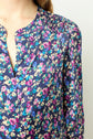 A person wearing a long-sleeved blouse with a colorful motif floral pattern in blue, pink, purple, and cream tones. The blouse features a split neckline and gathered detailing at the shoulder.