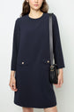 Woman wearing a navy blue, microfibre long-sleeve robe courte with two front pockets and boutons dorés, holding a black crossbody bag with a gold buckle.