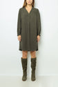 Woman wearing a knee-length, long-sleeve robe droite kaki with subtle jacquard pattern, V-neckline, and matching olive green knee-high boots, standing against a plain light background.