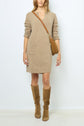 A woman wears a tan knit sweater dress with front pockets, knee-high brown suede boots, and a brown crossbody bag, standing against a plain white background.