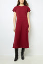 A woman wearing a short-sleeve, knee-length burgundy robe midi cintrée with black knee-high boots stands against a plain white background, exuding silhouette glamour.