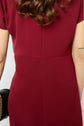 A person with wavy brown hair wears a short-sleeved, dark red robe midi cintrée, radiating silhouette glamour. Their arm shows a partial tattoo, and they hold a black clutch with a gold chain. Only their back and part of their arm are visible.
