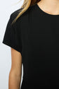 A close-up of a person wearing a robe noire cintrée with short sleeves, showing the shoulder, sleeve, and part of the chest; long blonde hair is partially visible.