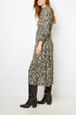 Woman wearing a robe longue à motif floral with a col lavallière and black, knee-high, heeled boots, standing against a white background.