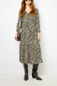 Woman in a patterned robe longue with a motif floral and a chic col lavallière, paired with black knee-high boots and a dark crossbody bag, standing against a white background.
