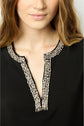 A woman with wavy light brown hair wears a black robe courte featuring a deep V-neckline adorned with intricate silver beading. Only the lower face and upper chest are visible.
