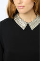 Close-up of a woman with long reddish-brown hair wearing a black top adorned with a shiny, silver strass-textured col chemise. Only the lower part of her face and upper torso are visible.