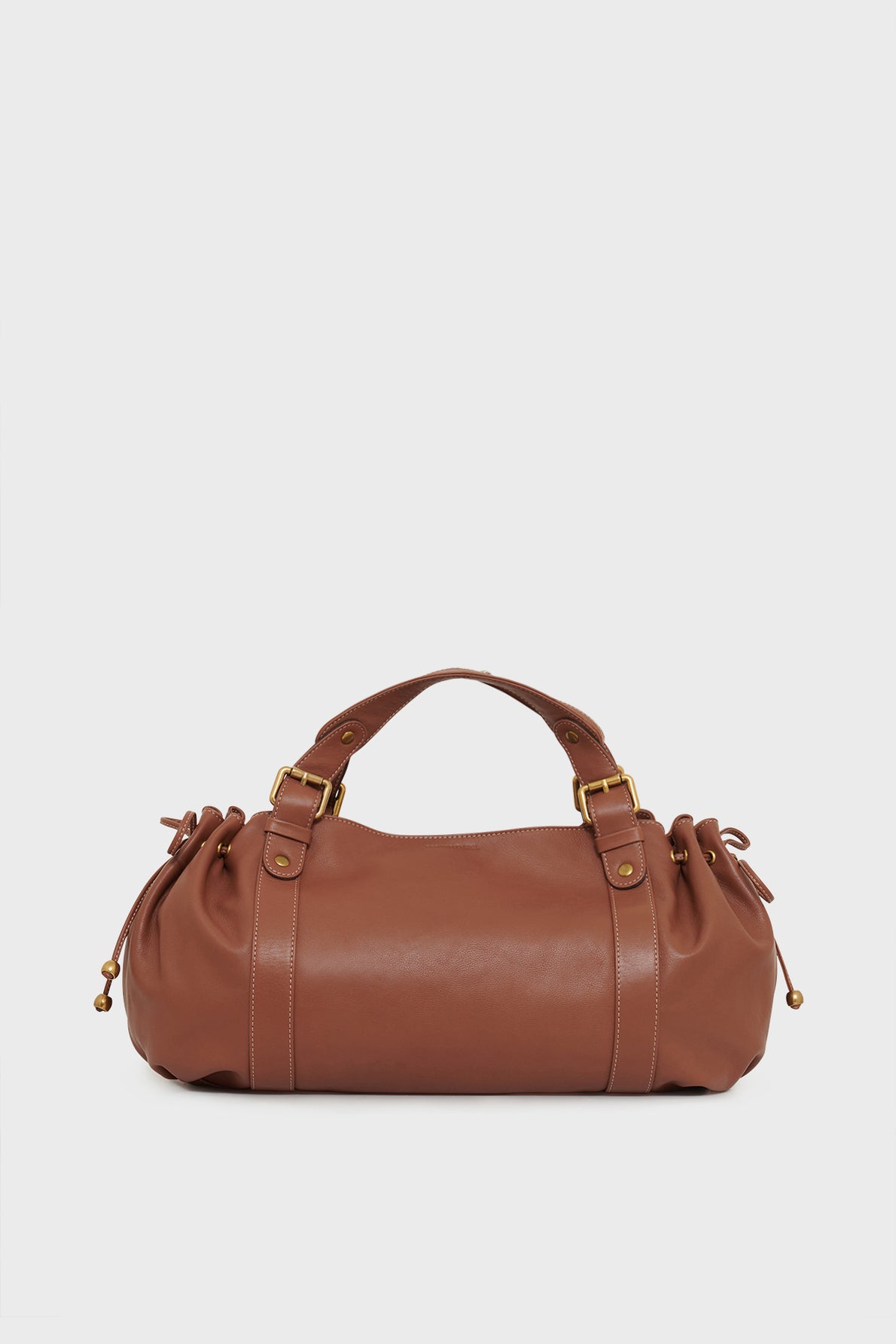 A brown leather duffel-style sac à main with gold hardware, two short handles, and gathered side details, crafted from cuir délicat and set against a plain white background.