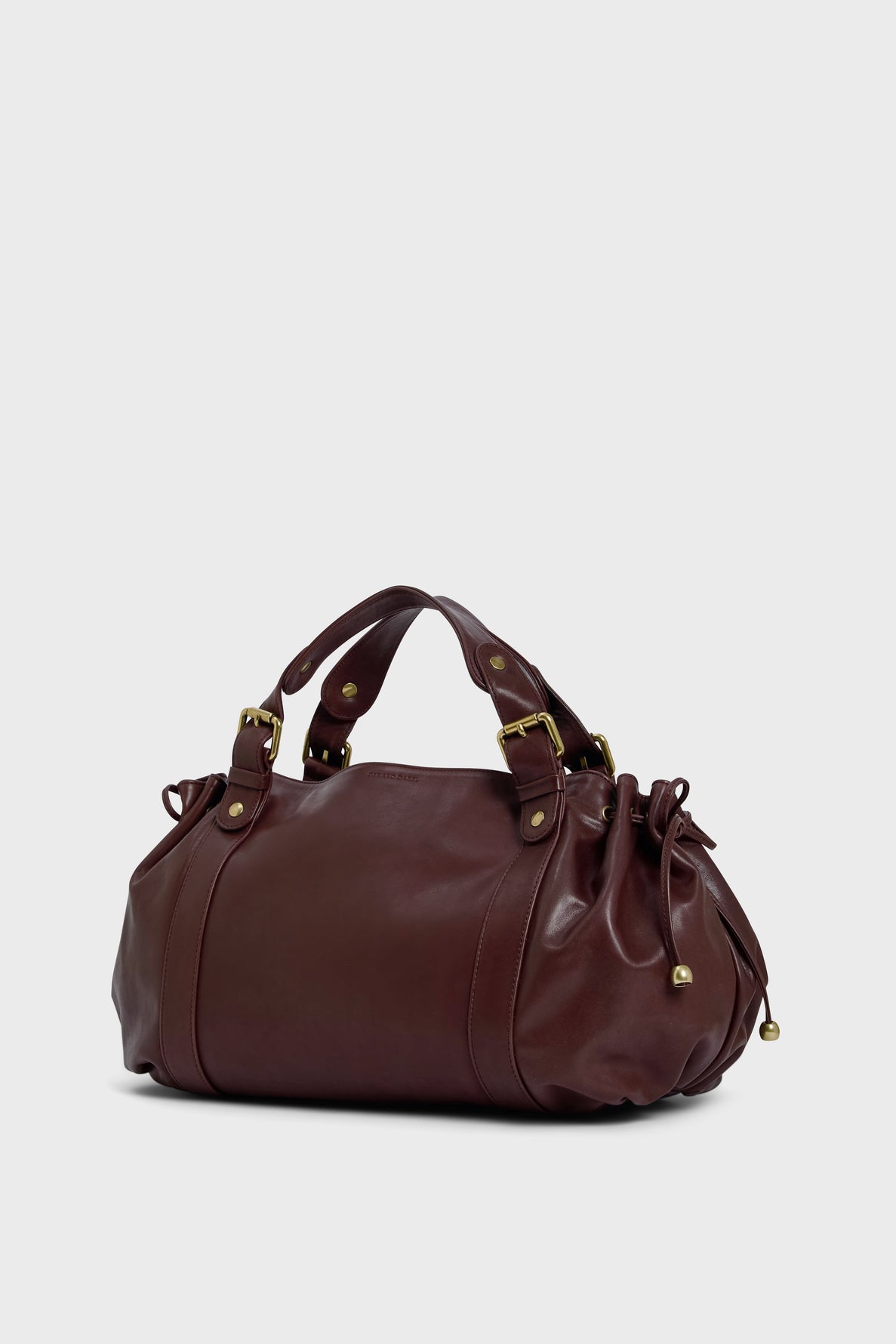 A brown leather sac à main with gold-toned hardware, short handles, and a drawstring detail on the sides, crafted in cuir délicat and echoing the refined spirit of maroquinerie Darel, set against a plain light gray background.