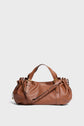 A brown Gerard Darel sac à main crafted from cuir grainé, featuring a curved shape, gold hardware, double handles, and an adjustable shoulder strap, set against a plain light background.