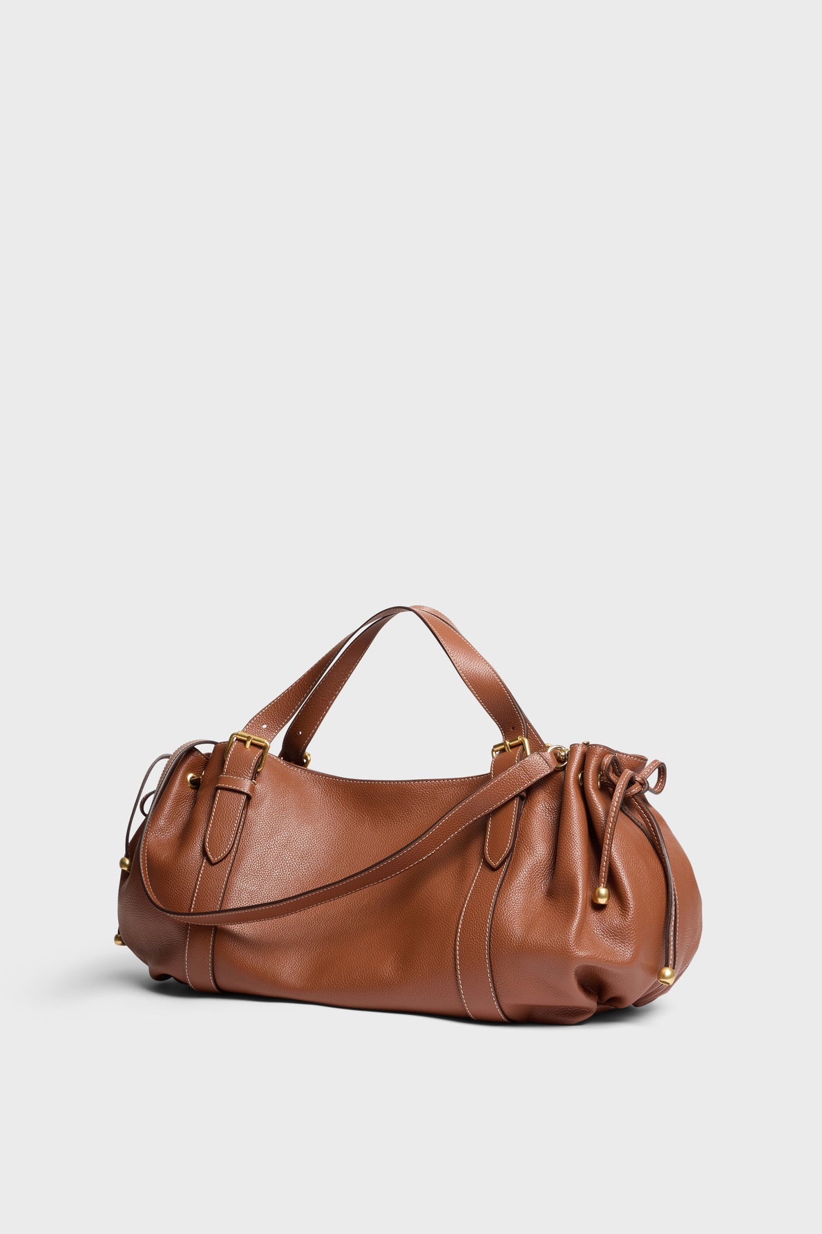 A brown cuir grainé leather sac à main with short handles, a long shoulder strap, and a drawstring detail on one end, displayed on a plain white background.