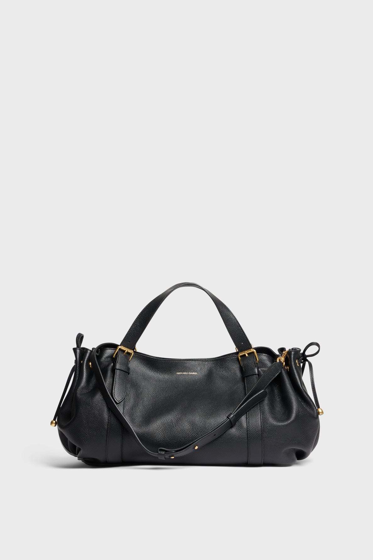 A black Gerard Darel sac à main in cuir grainé with gold hardware, dual handles, and an adjustable shoulder strap is displayed against a plain light gray background.