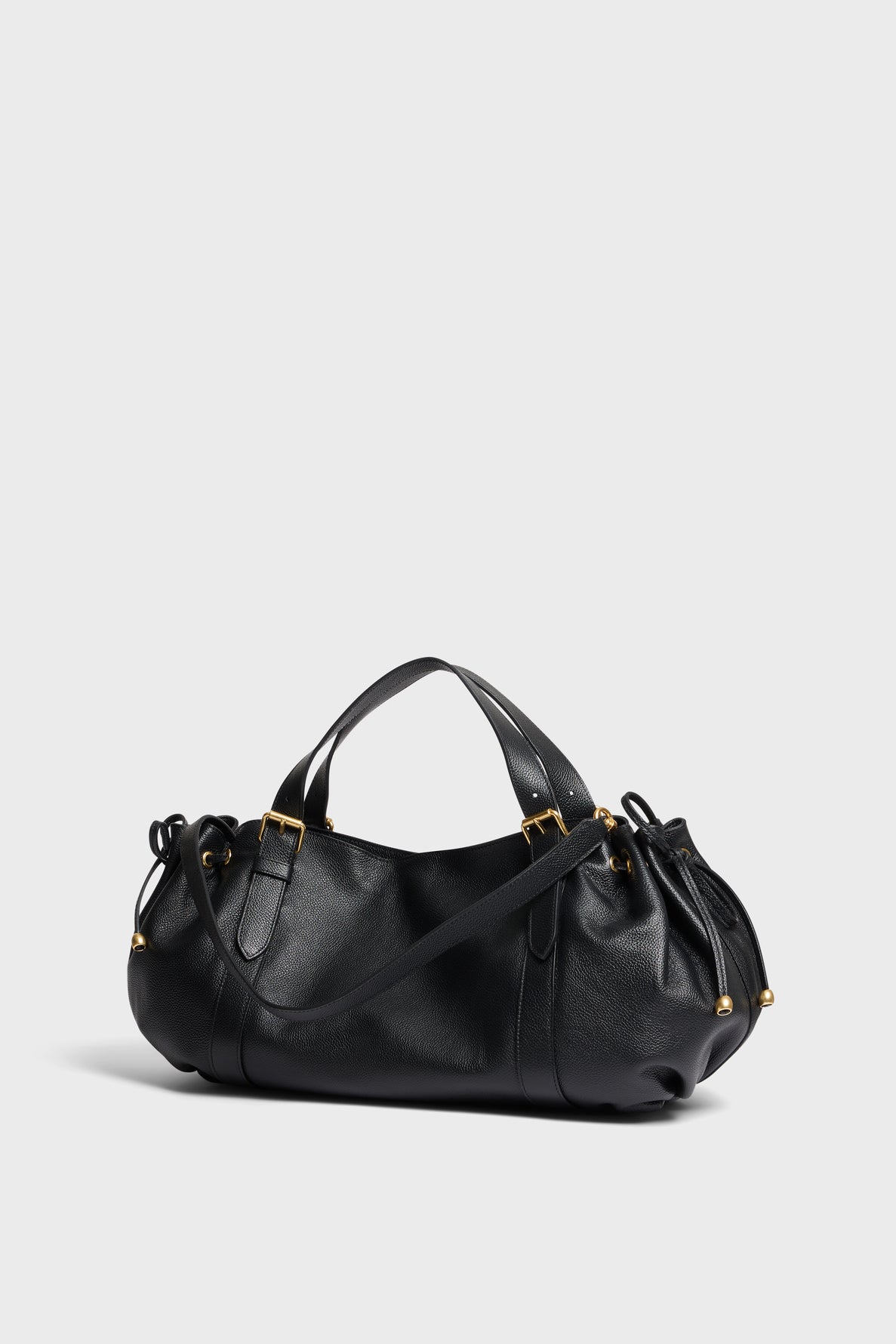 A black Gerard Darel sac à main in cuir grainé with gold hardware, featuring two top handles and a long adjustable shoulder strap, displayed on a plain light gray background.
