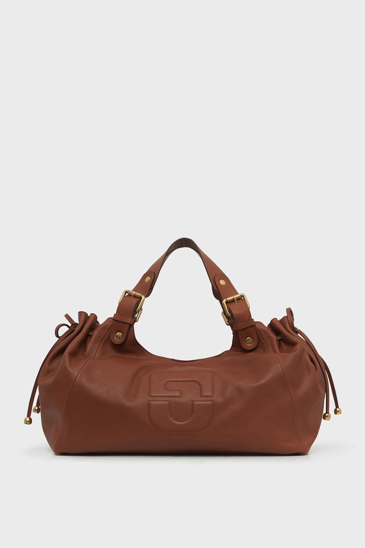 Brown leather sac à main with gold hardware, dual handles, drawstring sides, and an embossed logo on the front, set against a plain white background.