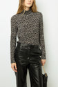 A person wearing a black and white floral long-sleeve mock-neck top with high-waisted black leather pants, holding a black handbag with a gold chain strap.