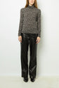 A person wearing a black and white patterned turtleneck top and black leather pants stands against a plain white background.