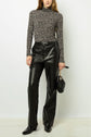 A person wearing a black and white floral turtleneck, black leather pants, black boots, and holding a black handbag stands against a plain white background.
