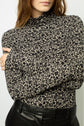 A woman wearing a black and white floral turtleneck top with long sleeves, paired with high-waisted black pants. Her arms are crossed, and her face is partially visible.