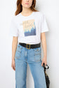 Woman wearing a white t-shirt en coton with a motif sérigraphié “with love” graphic, high-waisted blue jeans with large front pockets, and a black belt with a gold buckle, holding a black handbag.