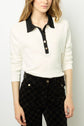 A woman wearing a polo blanc en coton with a col noir and black button placket, paired with high-waisted black patterned pants, stands against a plain background.