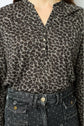 A person wears a T-shirt imprimé léopard with a buttoned col tunisien and high-waisted black jeans featuring a spotted pattern and visible buttons.