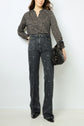 Woman wearing a T-shirt imprimé léopard à col tunisien, tucked into high-waisted dark jeans with a small white square pattern, holding a black handbag, standing against a plain white background. The top is crafted from coton mélangé for added comfort and style.