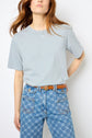 A person wearing a light blue t-shirt tucked into high-waisted blue jeans with a geometric pattern, accessorized with a brown belt, stands against a white background.