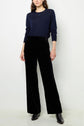A person wearing a long-sleeve navy top, black high-waisted wide-leg pants, and black ankle boots stands against a plain white background.