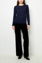 A person stands against a white wall wearing a navy blue long-sleeve top, black velvet wide-leg pants, and black shoes.
