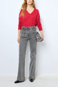 Woman standing against a white wall, wearing a rouge profond pull col V en cachemire, high-waisted gray jeans, black pointed shoes, and holding a metallic silver handbag by her side.