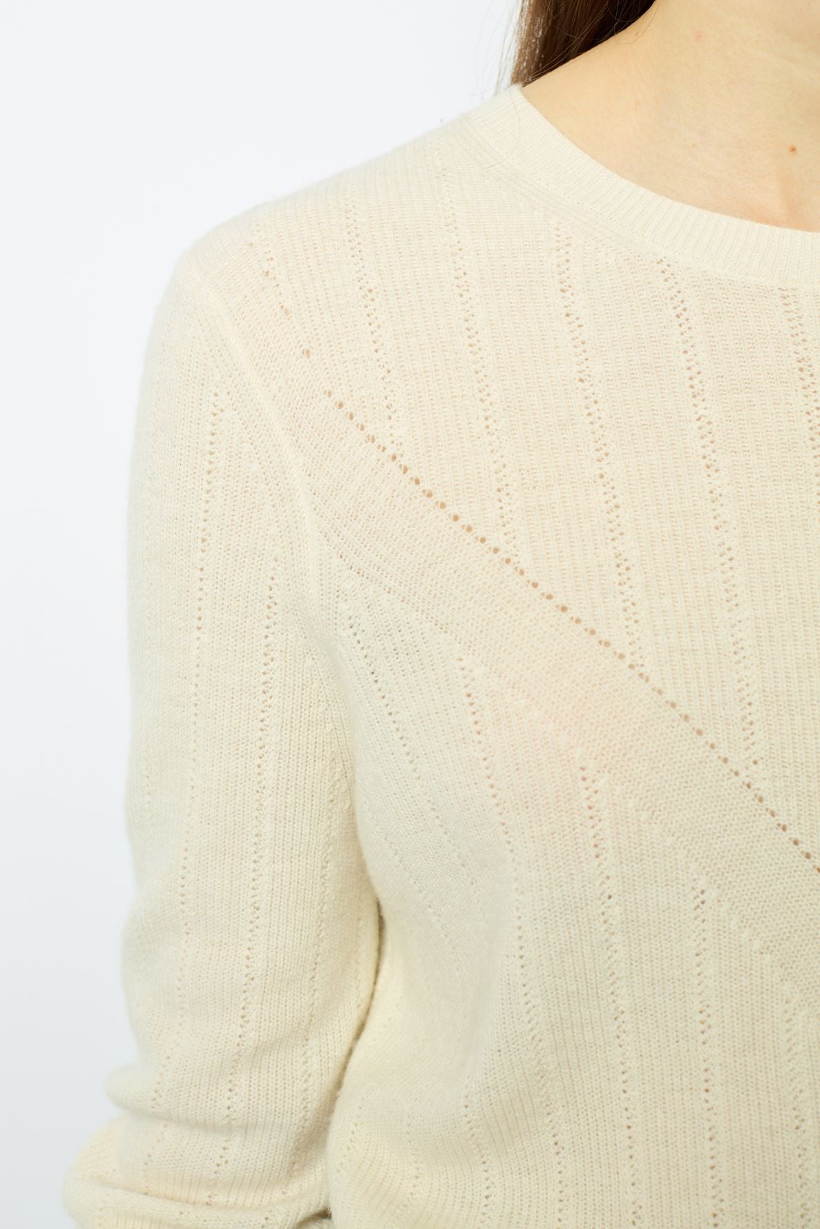 A close-up of a person wearing a cream-colored, ribbed knit sweater. Only part of the right shoulder, chest, and neck are visible. The background is plain and light.