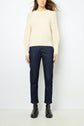 Woman wearing a cream knit sweater with textured sleeves, dark blue straight-leg jeans, and black ankle boots, standing against a plain white background.