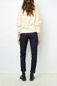 Woman standing with her back to the camera, wearing a cream sweater with textured sleeves, dark blue jeans, and black ankle boots against a plain white background.