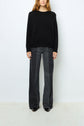 A person stands against a white background wearing a black sweater and high-waisted, wide-leg, faded black jeans with black shoes. Their face is partially out of frame.