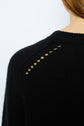 Close-up of a persons shoulder in a black knit sweater with small eyelet holes along the shoulder seam. The persons neck and part of their hair are visible against a plain background.