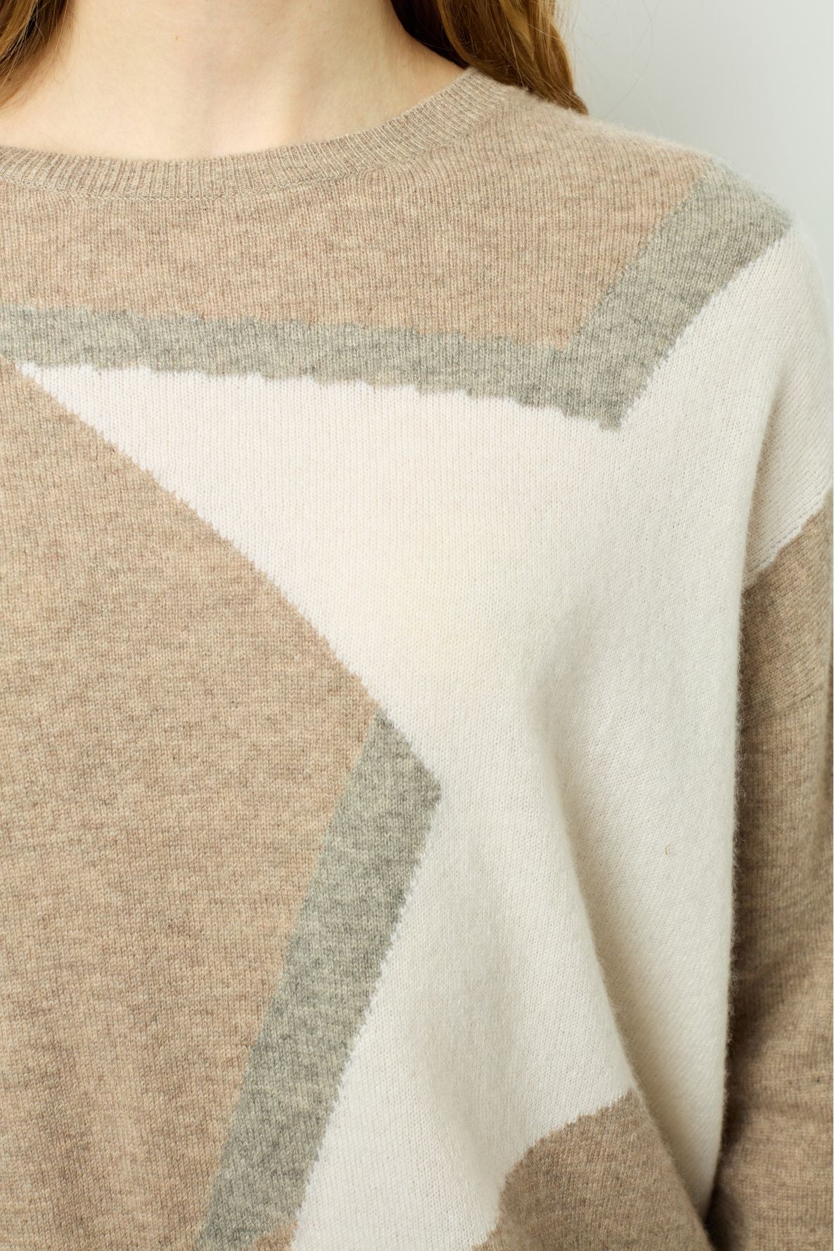 A close-up of a person wearing a beige, gray, and white geometric-patterned sweater. Only the lower part of their face, neck, and upper chest are visible.