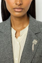 A woman wearing a grey blazer à chevrons and cream blouse with a fleur en strass brooch pinned to her lapel.