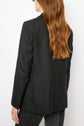 A person with long, wavy red hair is wearing a dark veste rayée, styled with dark jeans, standing with their back to the camera against a plain white background, effortlessly channeling un esprit tailleur.