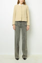 Woman wearing a beige, buttoned jacket over a white top and gray wide-leg jeans, standing against a plain white background. Only her body from neck to feet is visible.