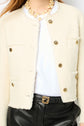 Person wearing a cream textured jacket with gold buttons, a white shirt, a chunky pearl necklace, and black leather pants with a gold-buckled belt. Their face is not visible.