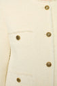 Close-up of a cream-colored textured jacket with four ornate gold buttons and two chest pockets.